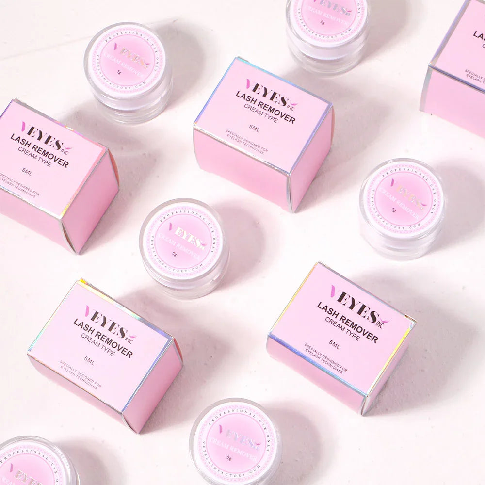 Multiple pink boxes and matching jars of eyelash extension cream remover on a flat surface.