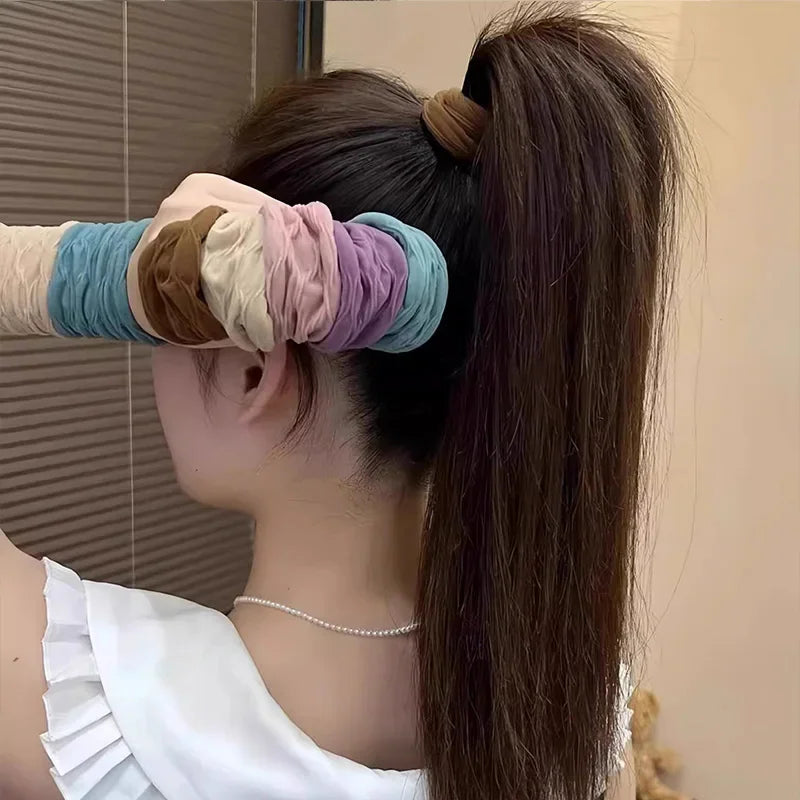 A woman holding a set of colorful fabric scrunchies near her high ponytail