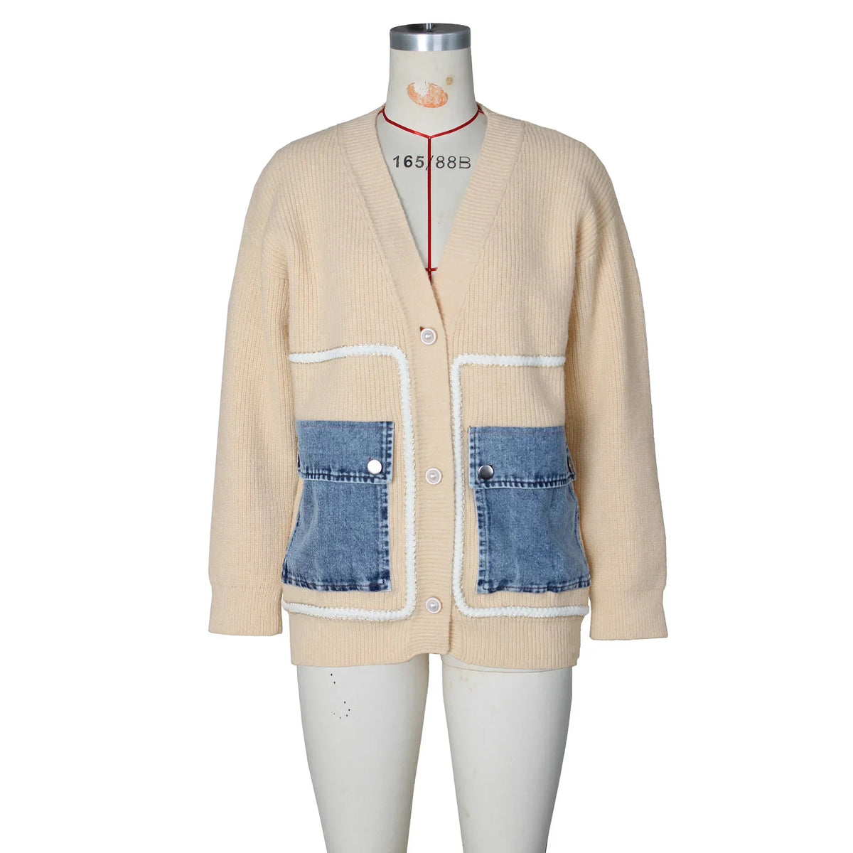 Front view of a beige knit cardigan with blue denim pockets and white stitching on a mannequin.
