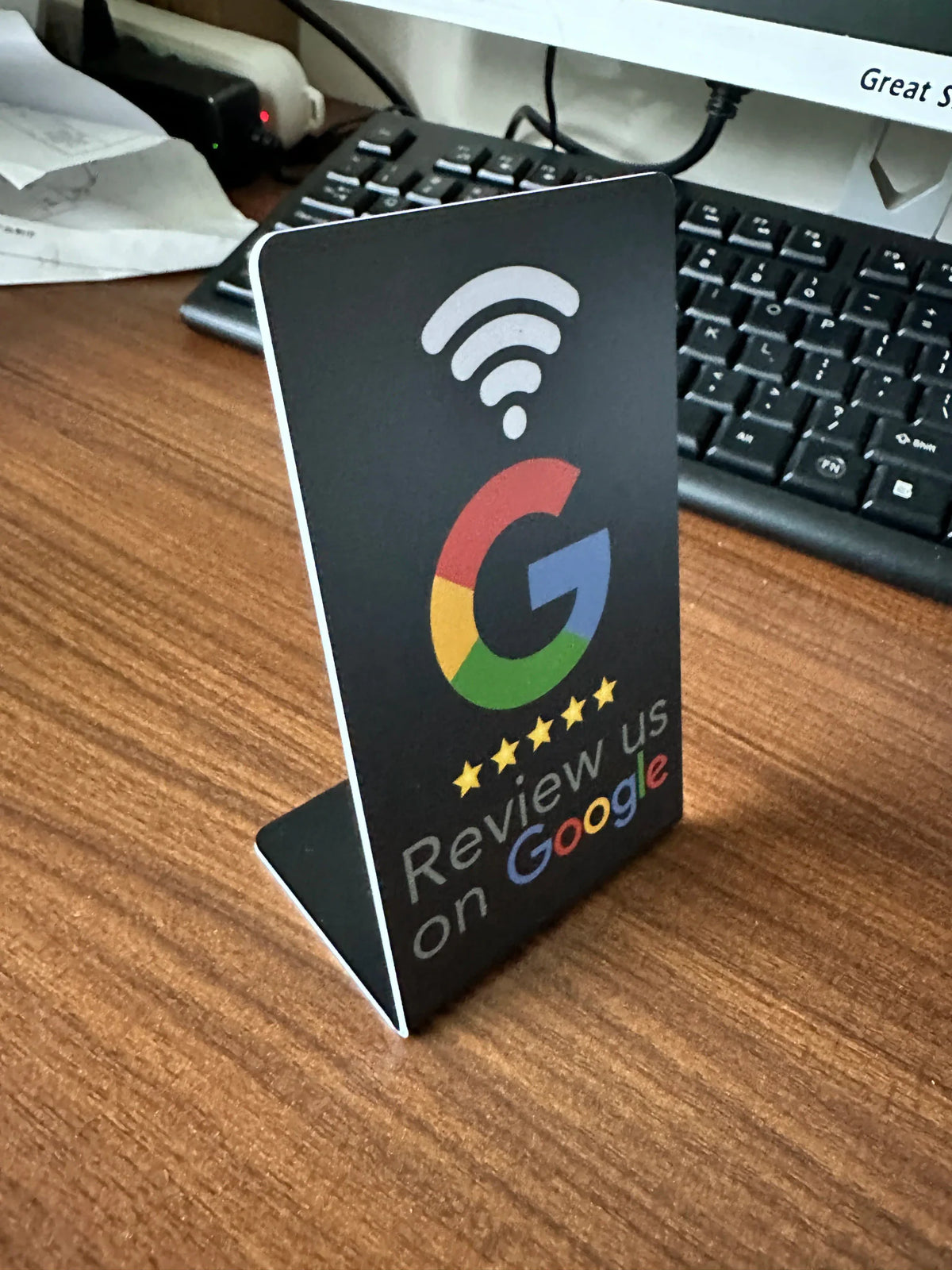 Black L-shaped NFC review stand with Google branding on a wooden desk