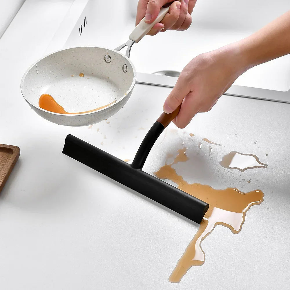 A black window wiper cleaning spilled liquid from a kitchen countertop surface