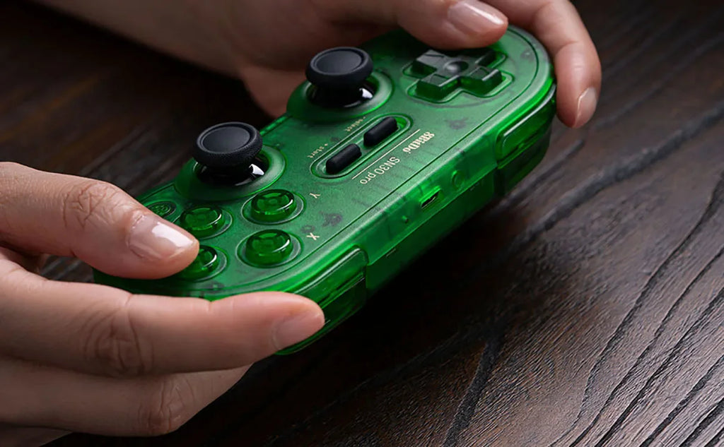 Hands holding a green transparent wireless game controller over a wooden surface.