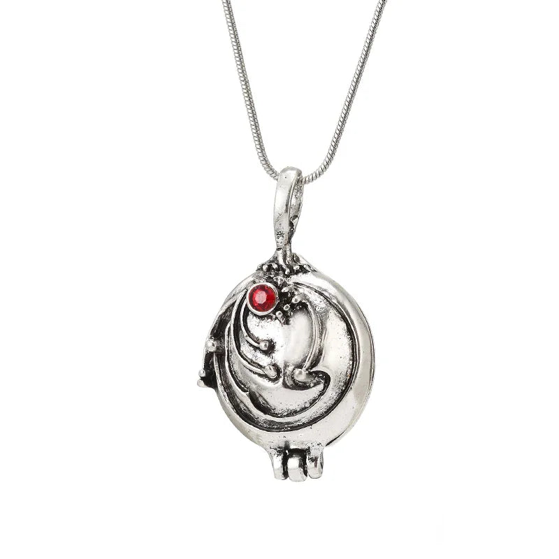 A silver locket pendant with a small red stone on a delicate chain.