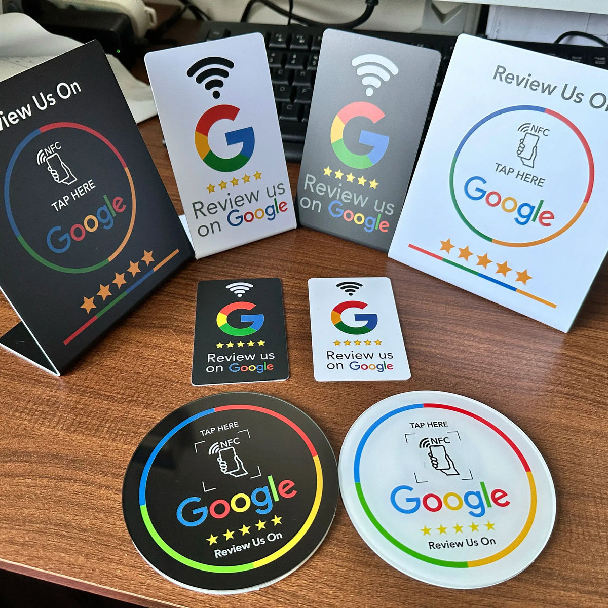 Assorted black and white NFC review stands and cards featuring Google review branding on a wooden desk surface