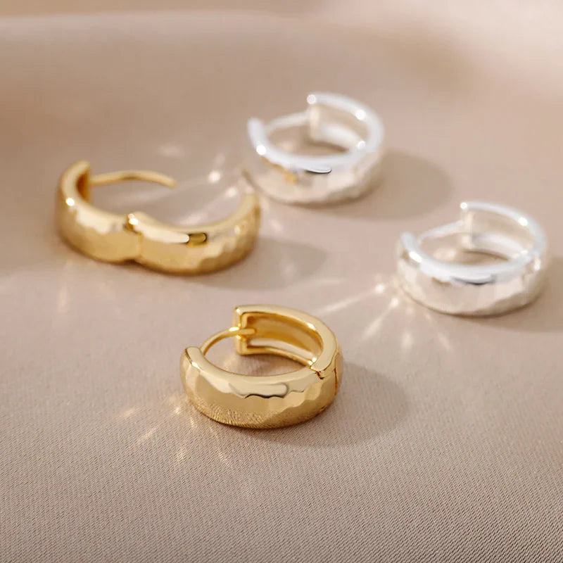 Two pairs of small hoop earrings in gold and silver tones on a neutral background