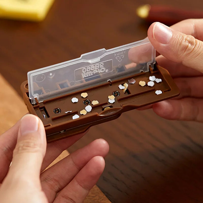 Hands opening a brown portable mini hole puncher containing paper hole cutouts.