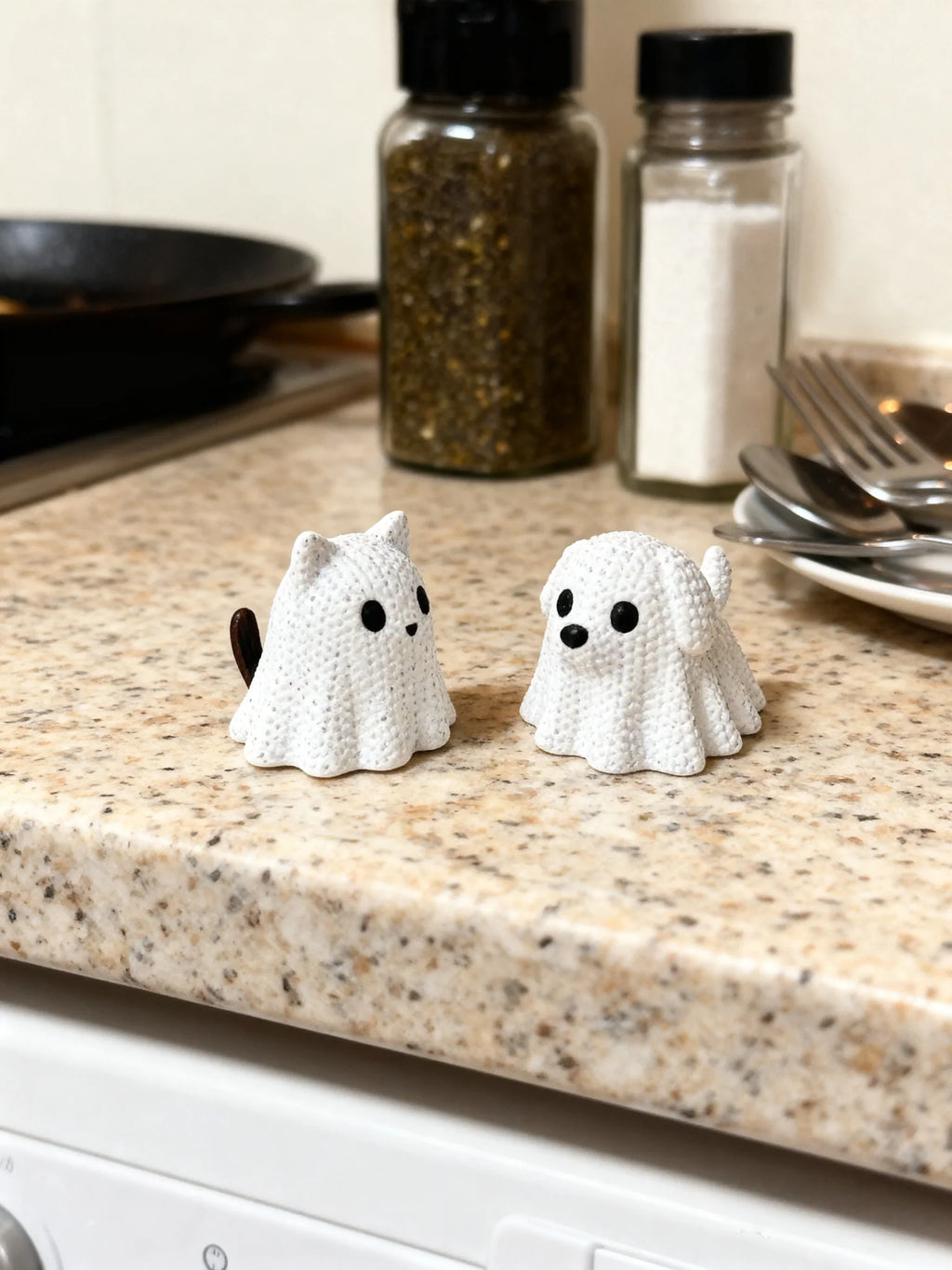 Small white ghost cat and ghost dog decorative statues sitting on a kitchen counter