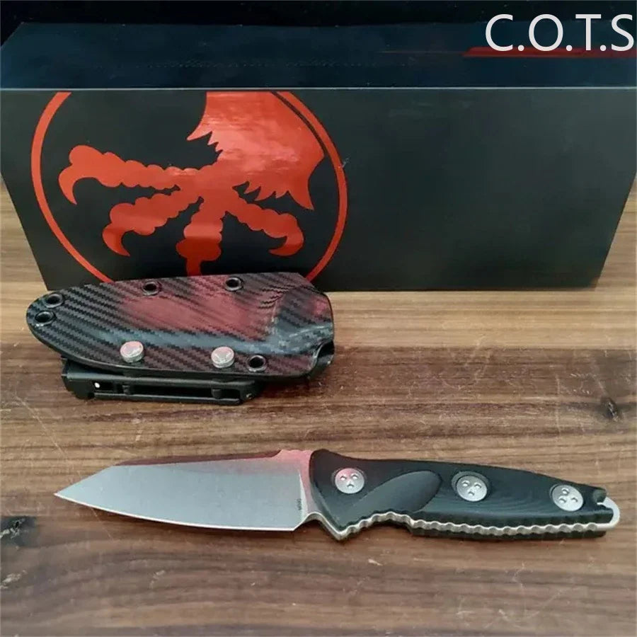 Fixed blade knife with black handle and Kydex sheath, displayed in front of a branded gift box.