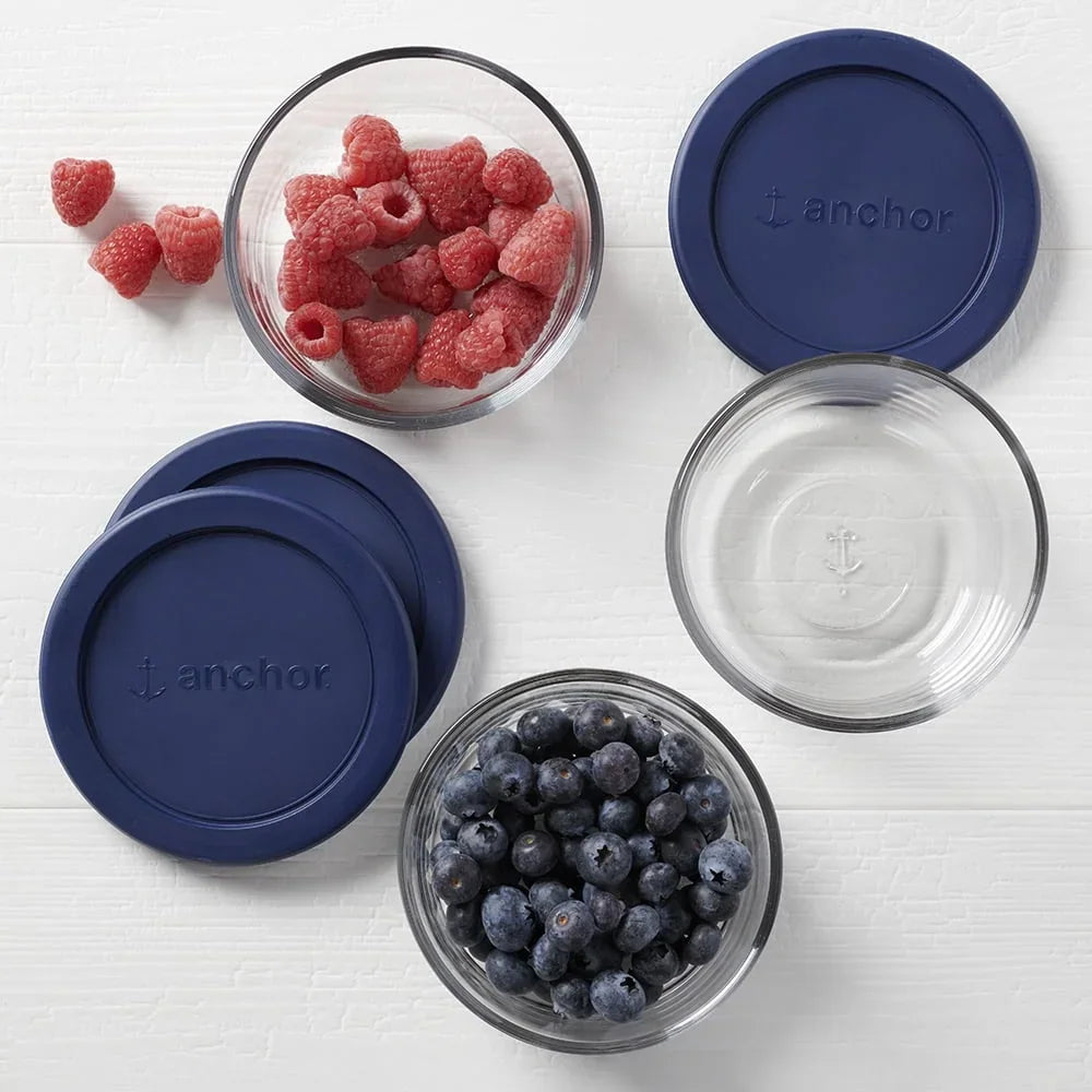 Round glass food storage containers with blue lids, some filled with blueberries and raspberries