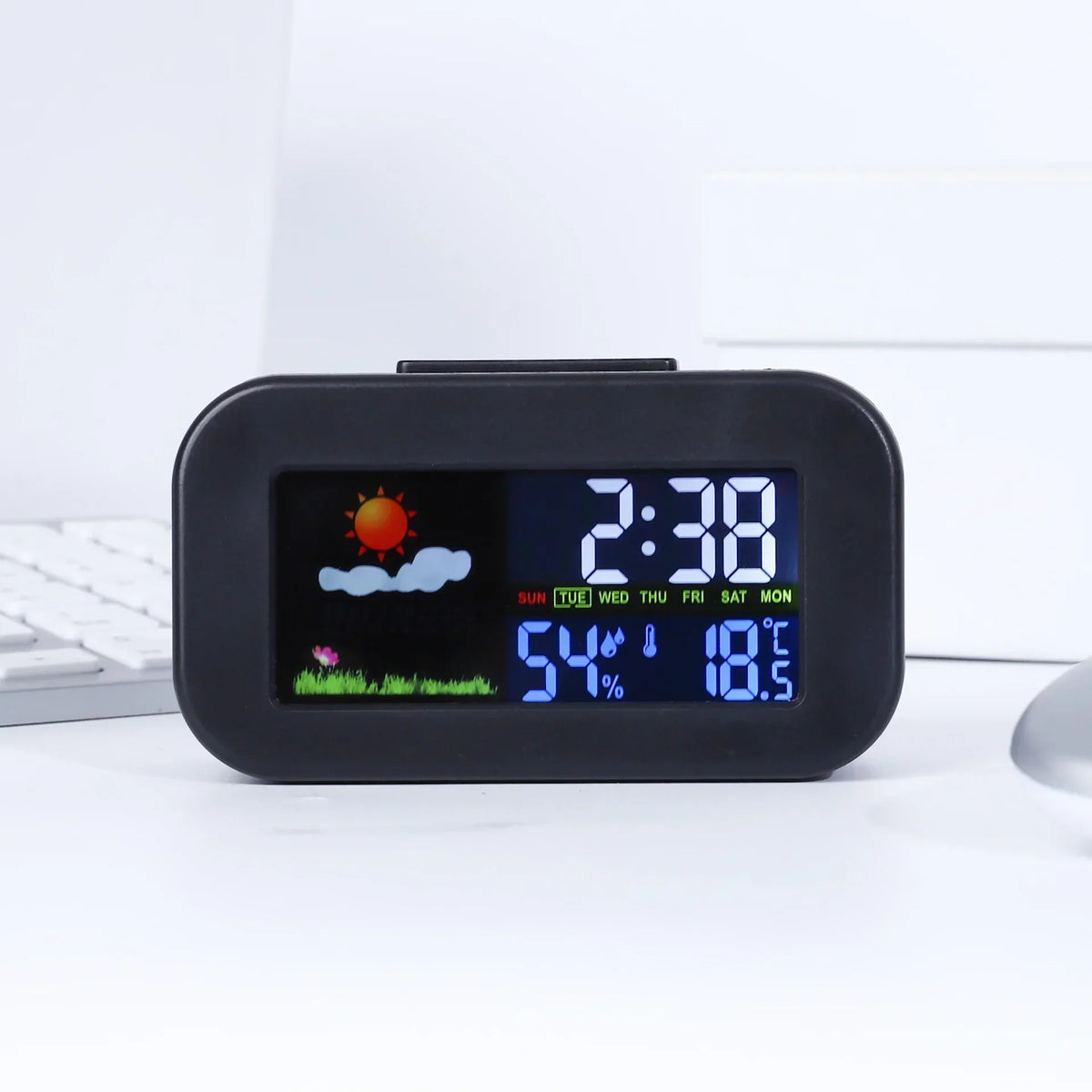 Digital weather station clock on a desk with white computer keyboard in background