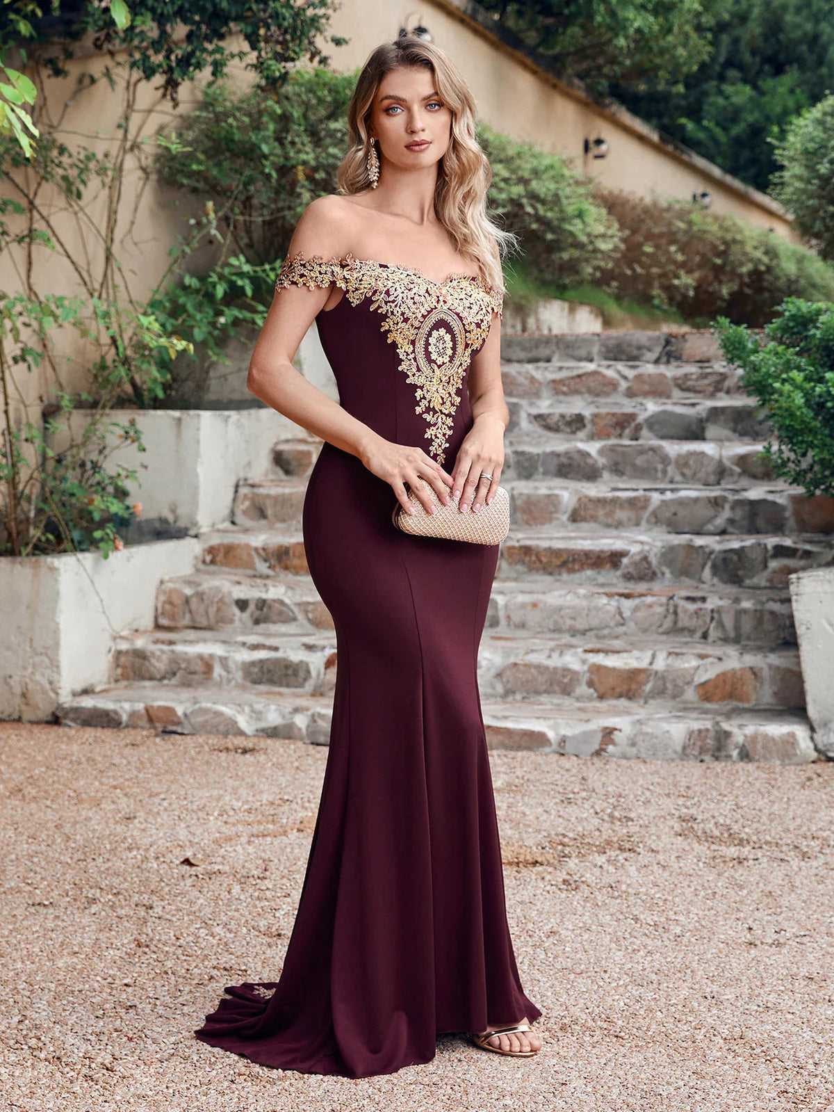 Burgundy formal mermaid dress with gold embroidery held by a model on stone steps