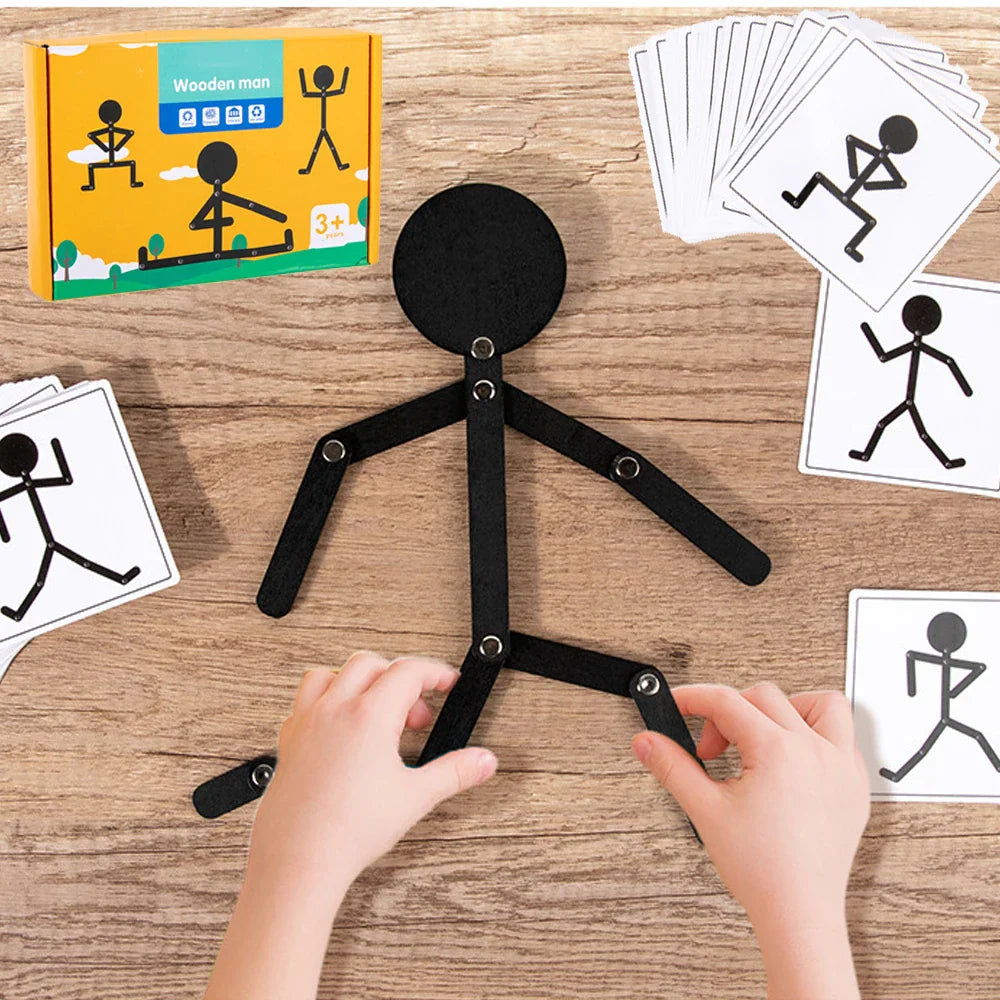 A black posable wooden stick figure toy on a wooden surface with matching pose cards and packaging.