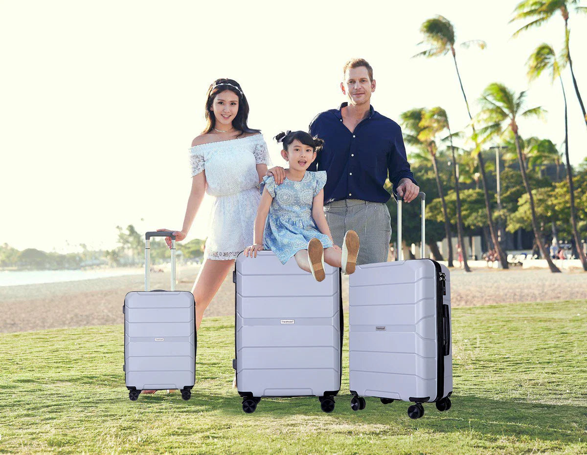 A family posing with light blue hardshell suitcases at the beach.
