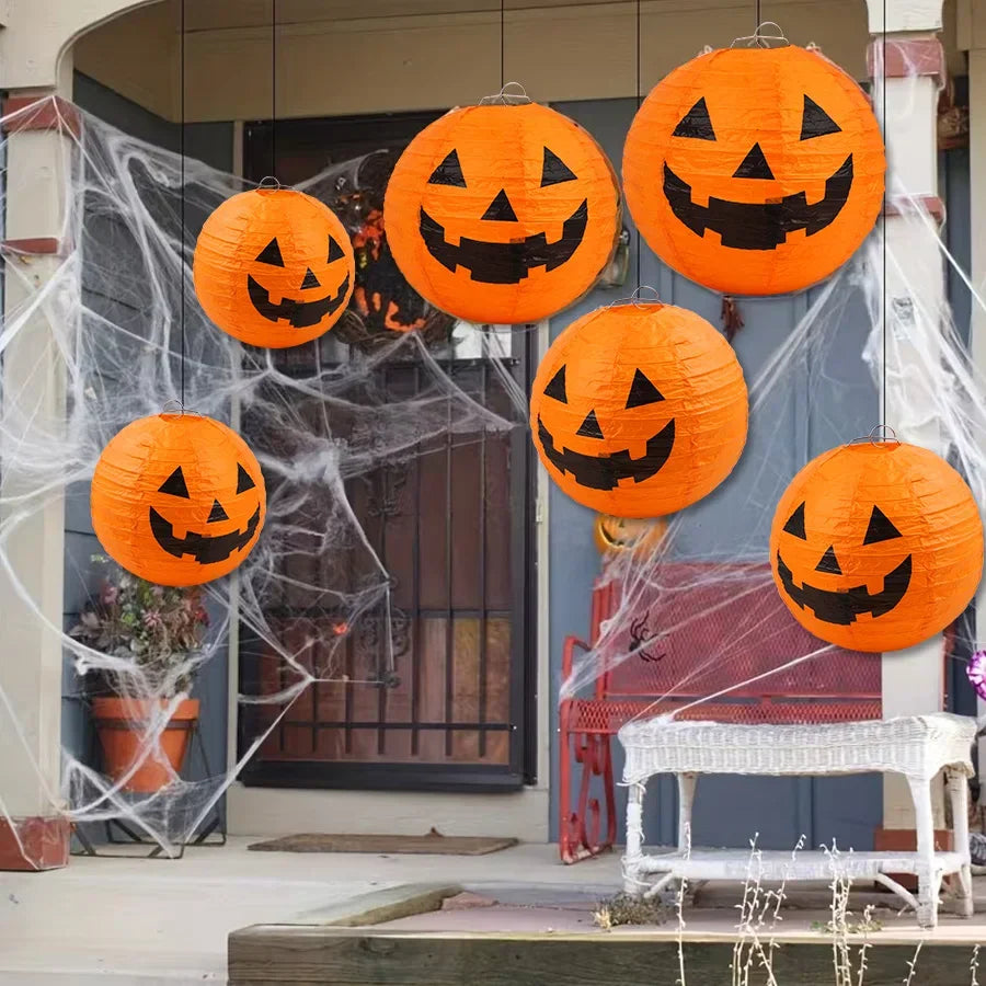 Hanging orange jack-o'-lantern paper lanterns in front of a house decorated with artificial spider webs