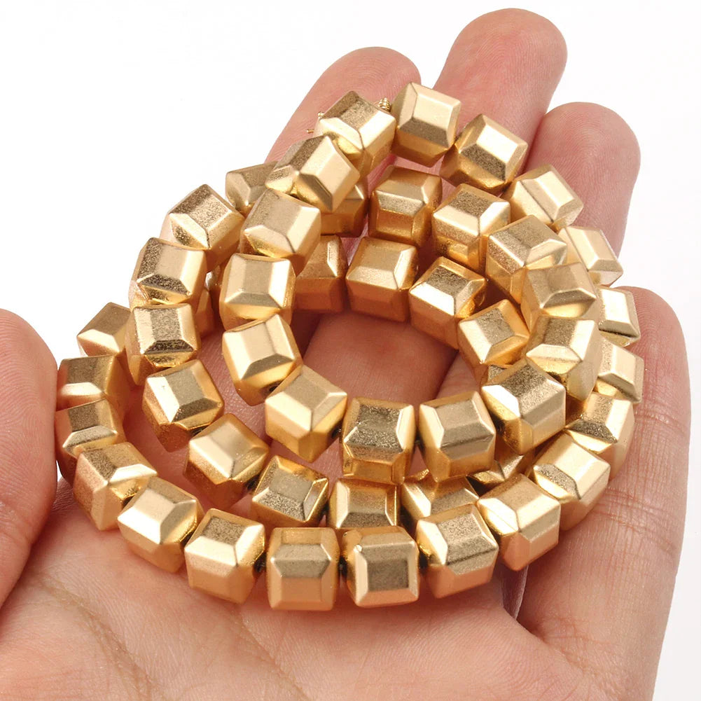 A hand holding a coiled strand of gold-plated square cube beads.