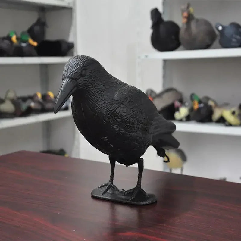A side view of a black crow bird deterrent figure, placed on a table.