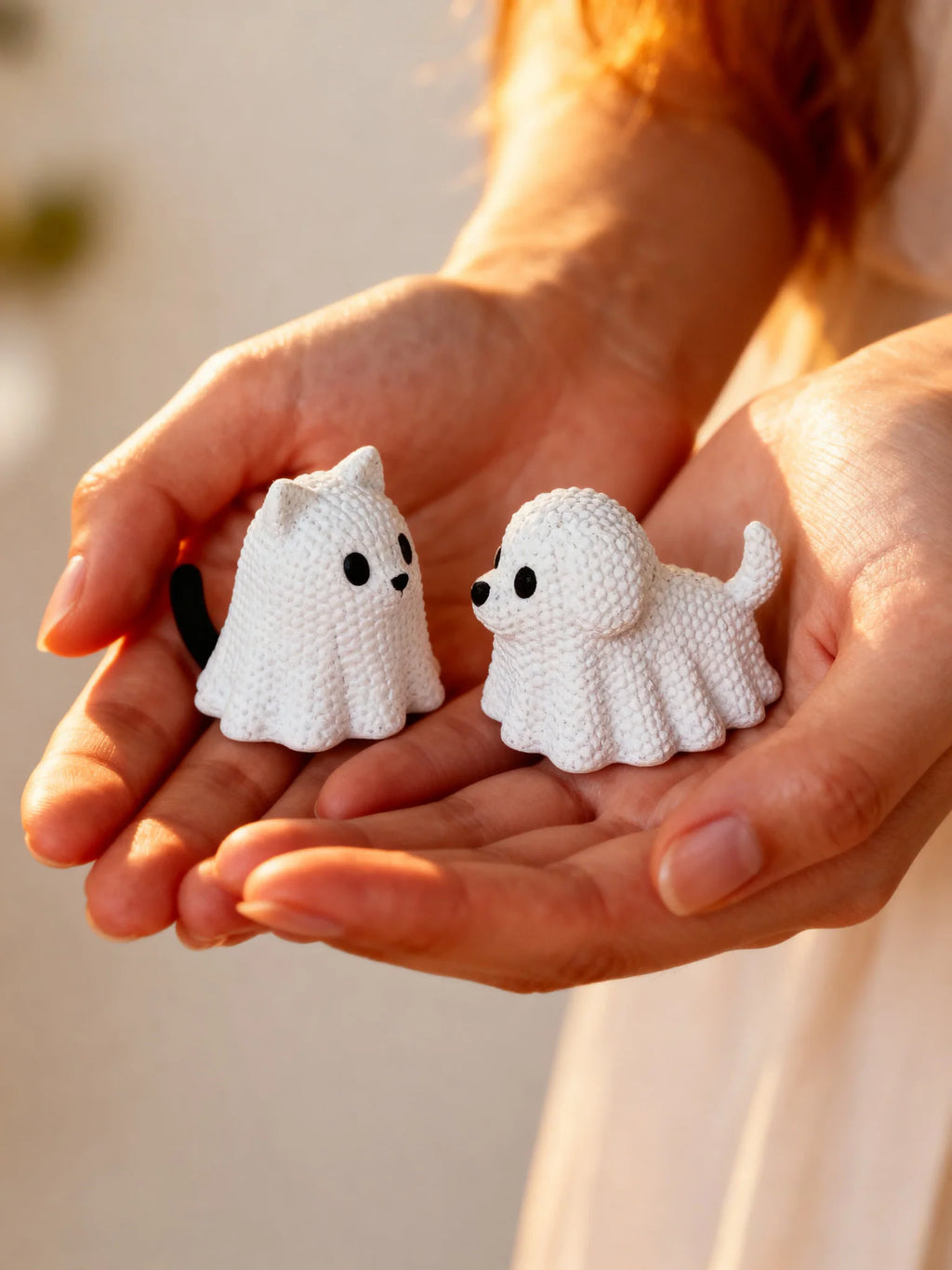 Set of two small white ghost cat and ghost dog figurines held in hands in warm sunlight