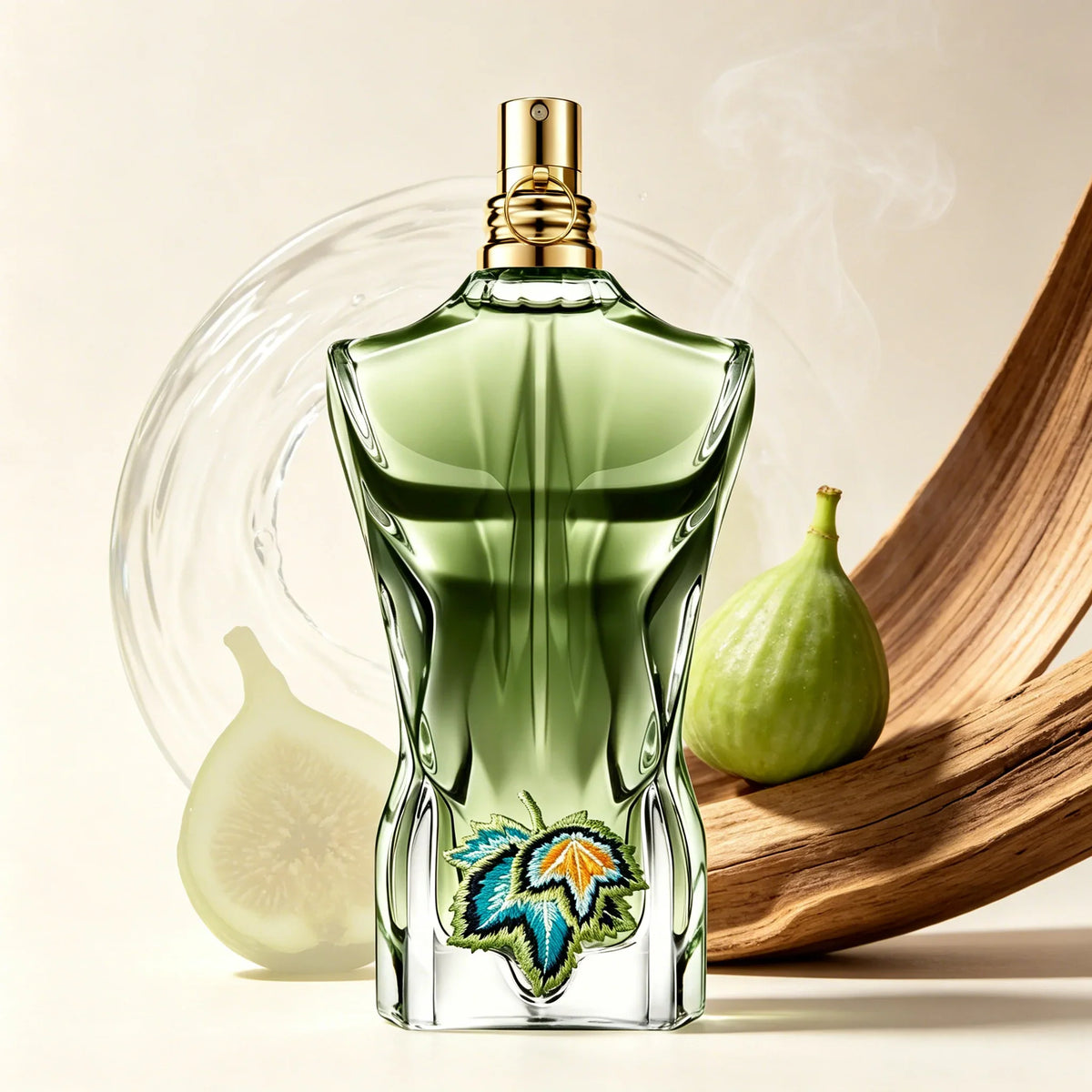Green torso-shaped glass perfume bottle with leaf embroidery placed next to a whole fig and piece of wood.