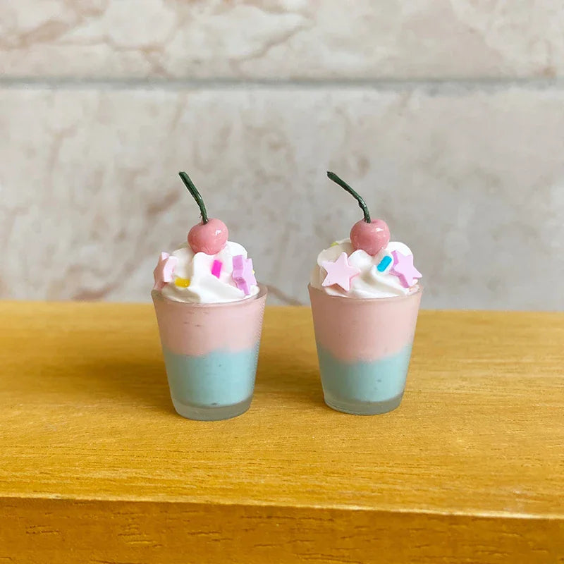 Two miniature dessert cups with pink and blue layers, whipped cream, sprinkles, and a cherry topper.