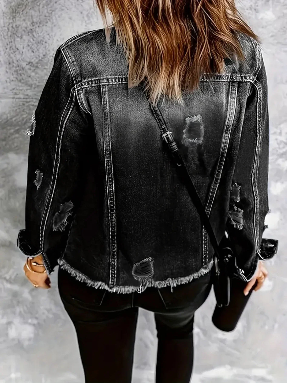 Back view of a person wearing a dark grey distressed denim jacket with frayed hem