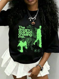 Model wearing black t-shirt with green graphic print, paired with a white skirt