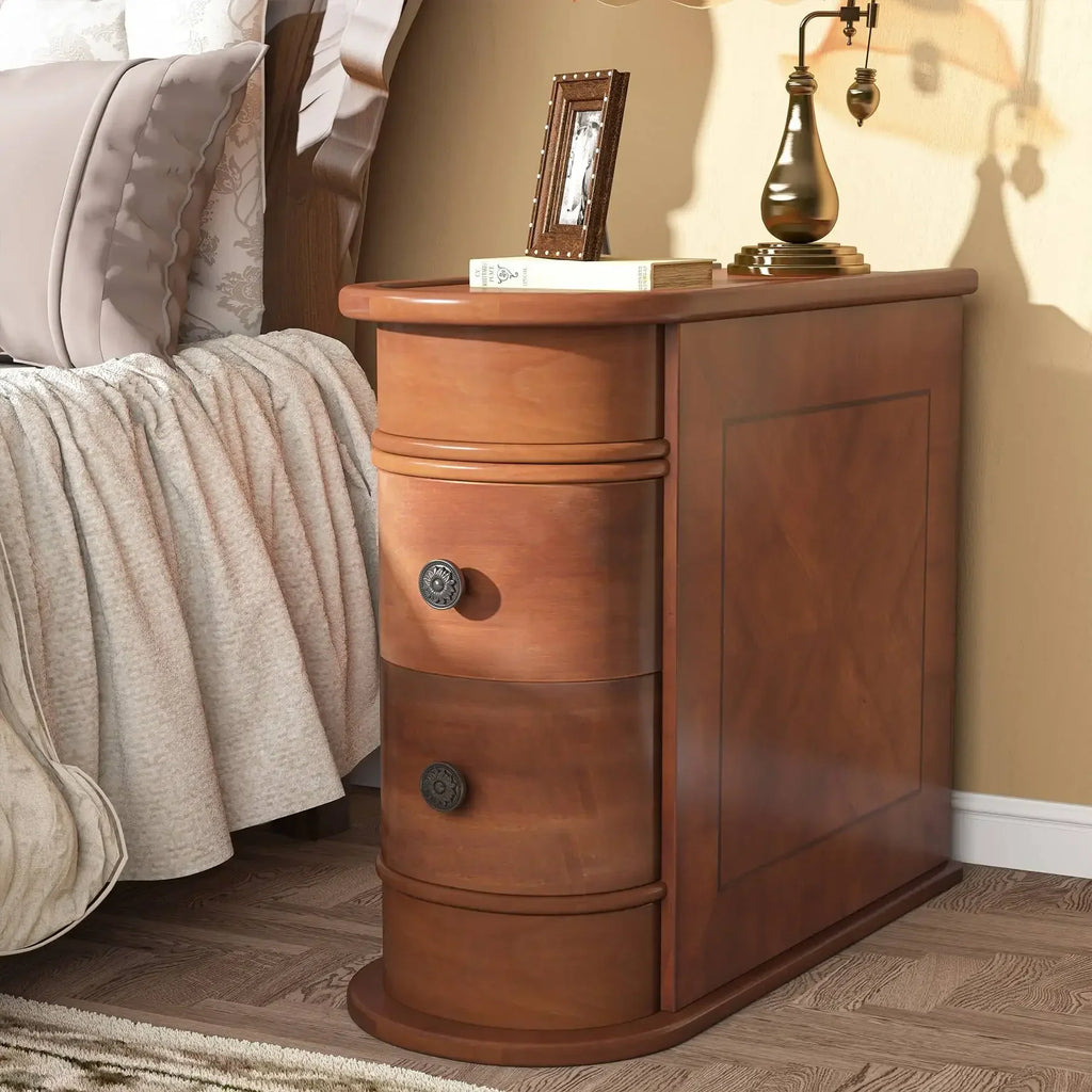 Narrow wooden bedside table with two drawers in a bedroom setting, featuring a table lamp and a framed picture on top