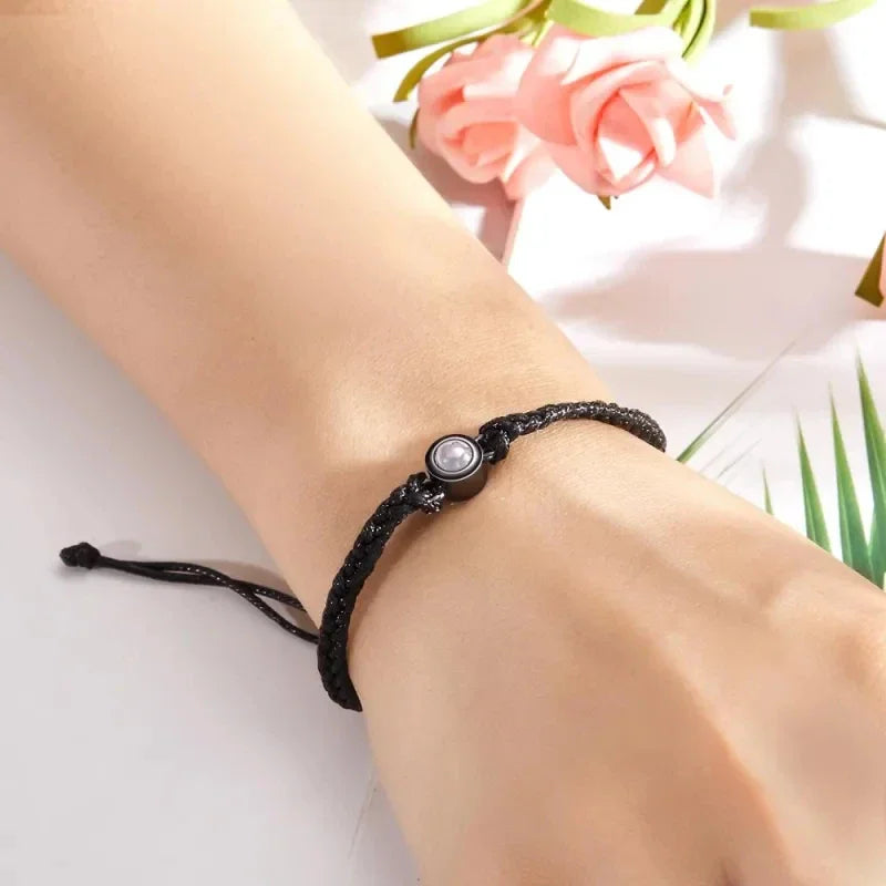 A black braided rope bracelet with a circular charm on a wrist.