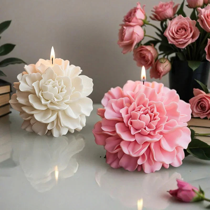 A white and a pink peony shaped candle burning on a table with a rose bouquet