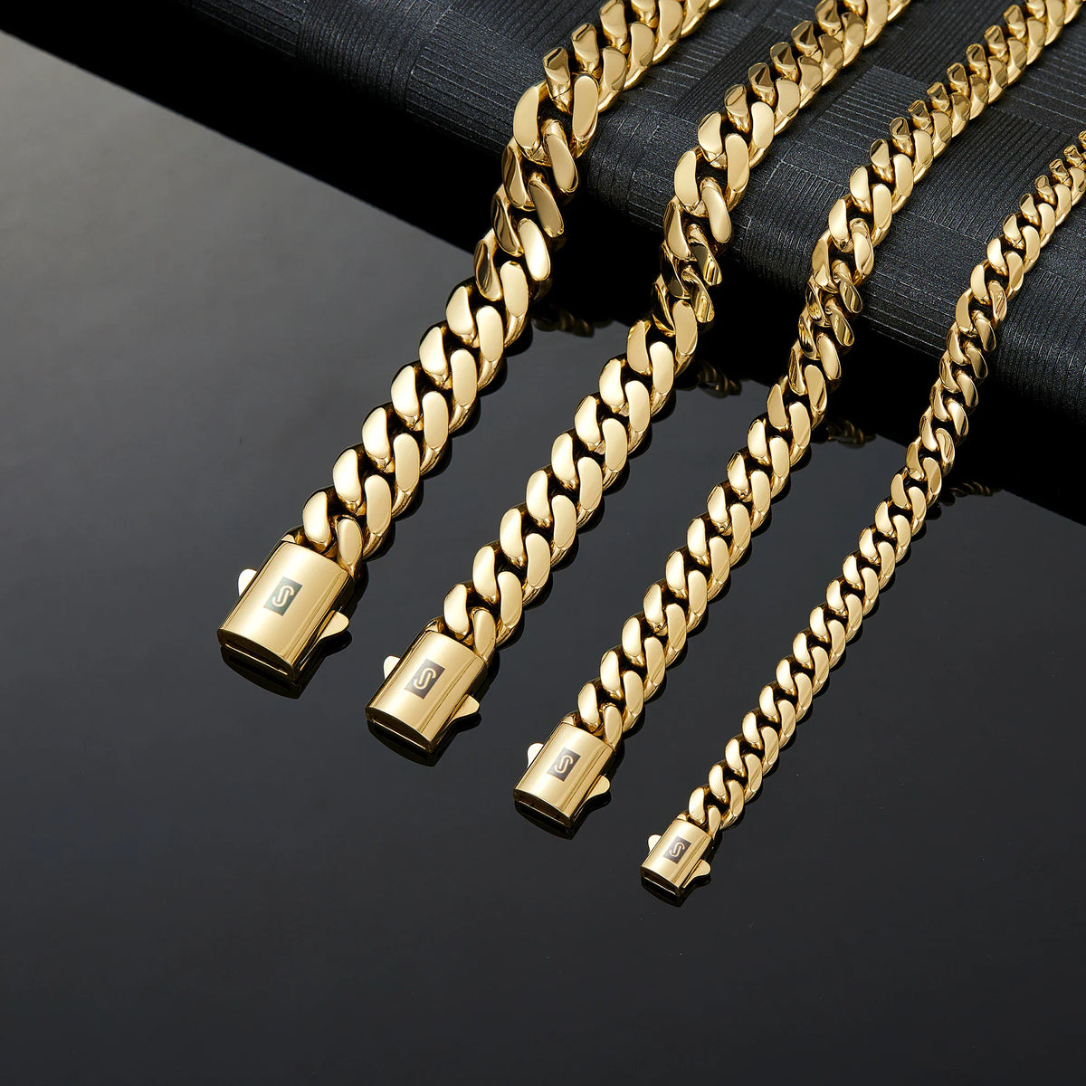 Four gold cuban link chains of different widths laid out on a black background