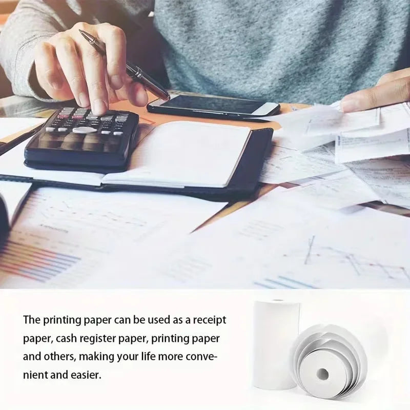 A person using a calculator and writing on paper with thermal paper rolls nearby