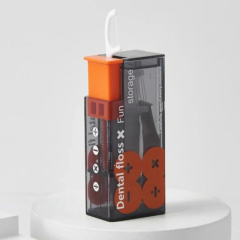 A vertical standing portable dental floss dispenser in grey and orange, showing the ejection mechanism.