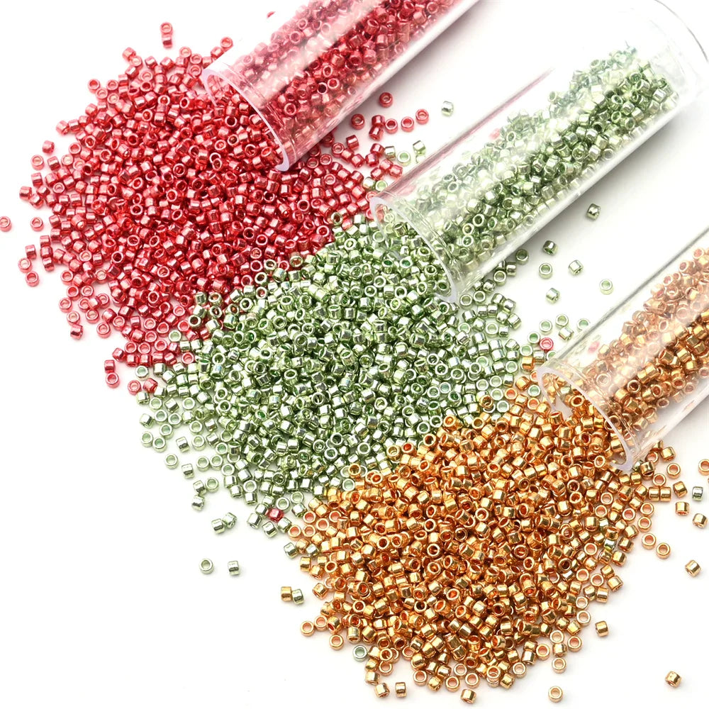 Three clear tubes spilling red, green, and gold metallic glass seed beads onto a white surface.