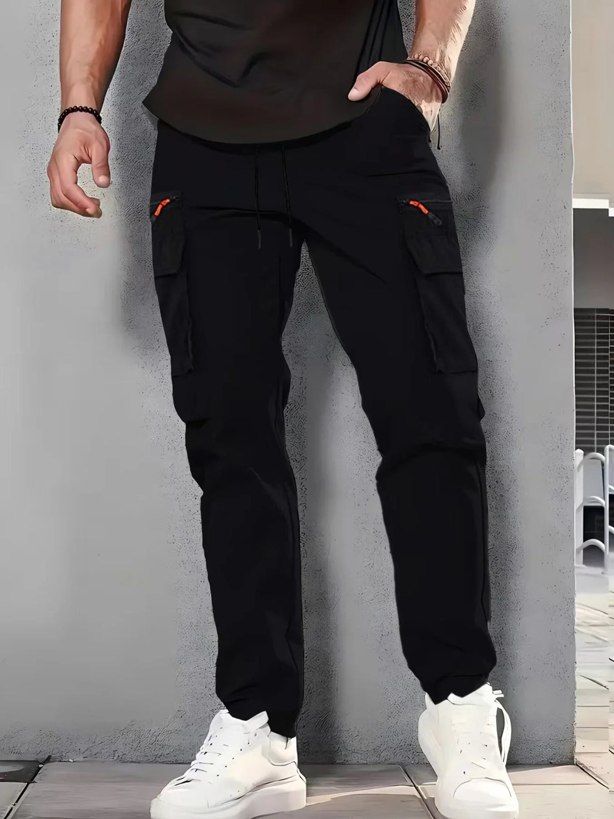 Man wearing black cargo pants with black zipper pockets and white sneakers.