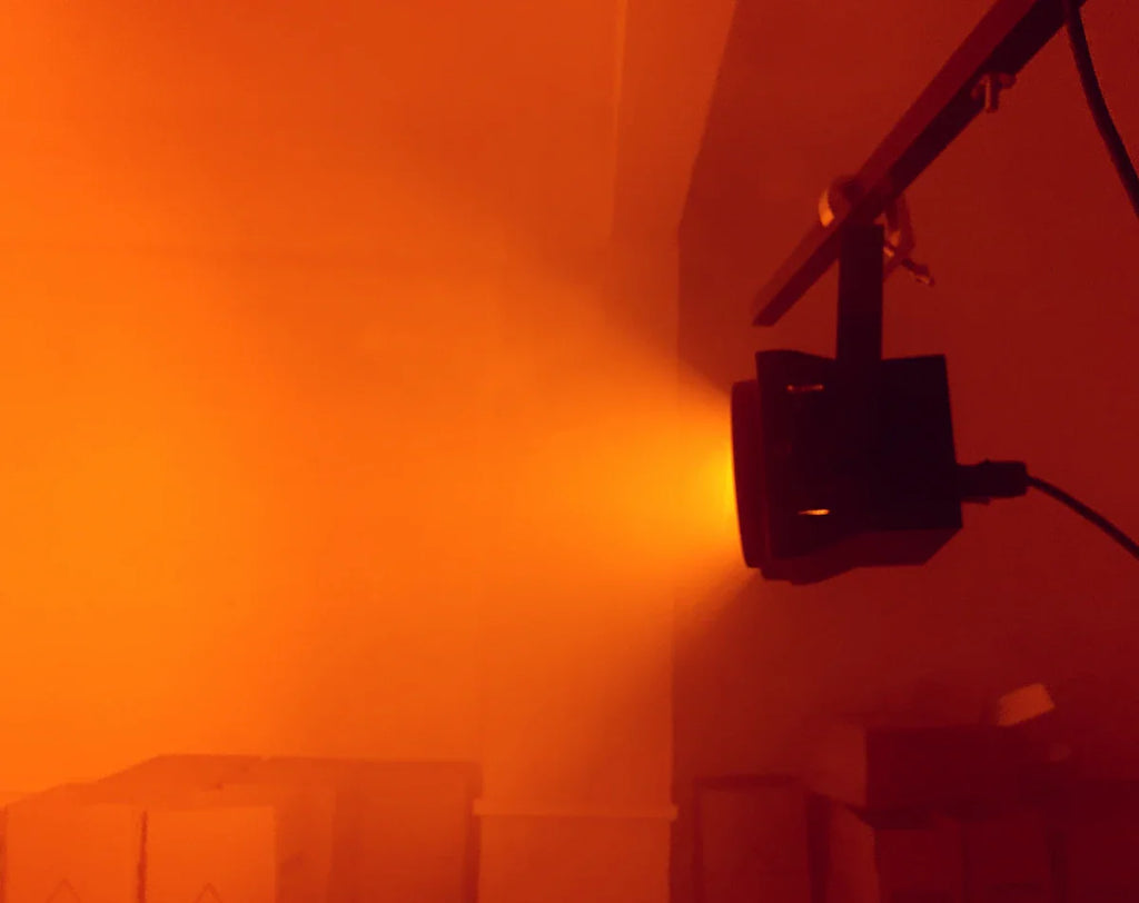 Black stage blinder light emitting an orange wash beam in a dark room