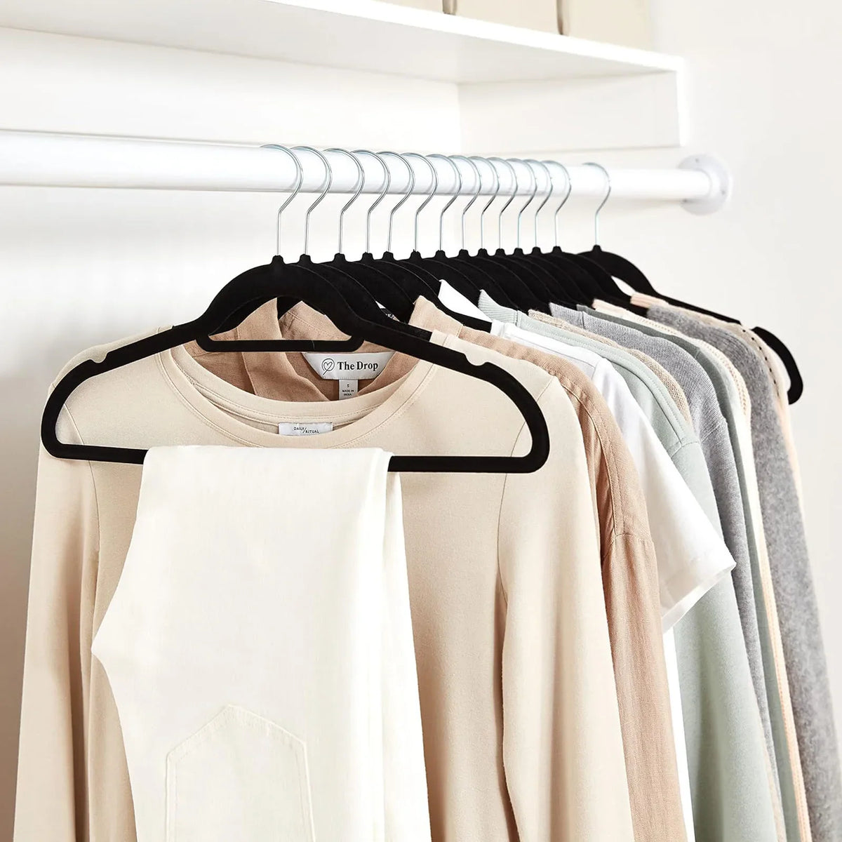 A row of black velvet hangers in a closet holding various clothes.