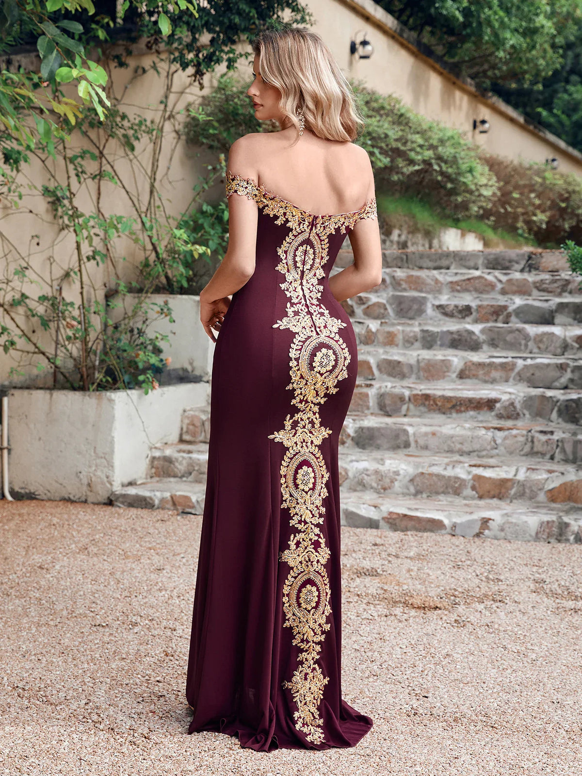 Back view of a burgundy mermaid gown with gold lace detail worn on stone stairs