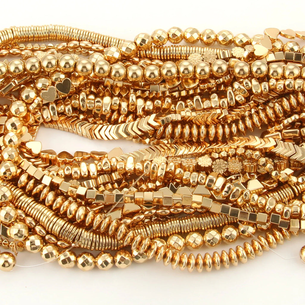 Multiple strands of gold-colored hematite beads in various shapes laid out flat on a surface.