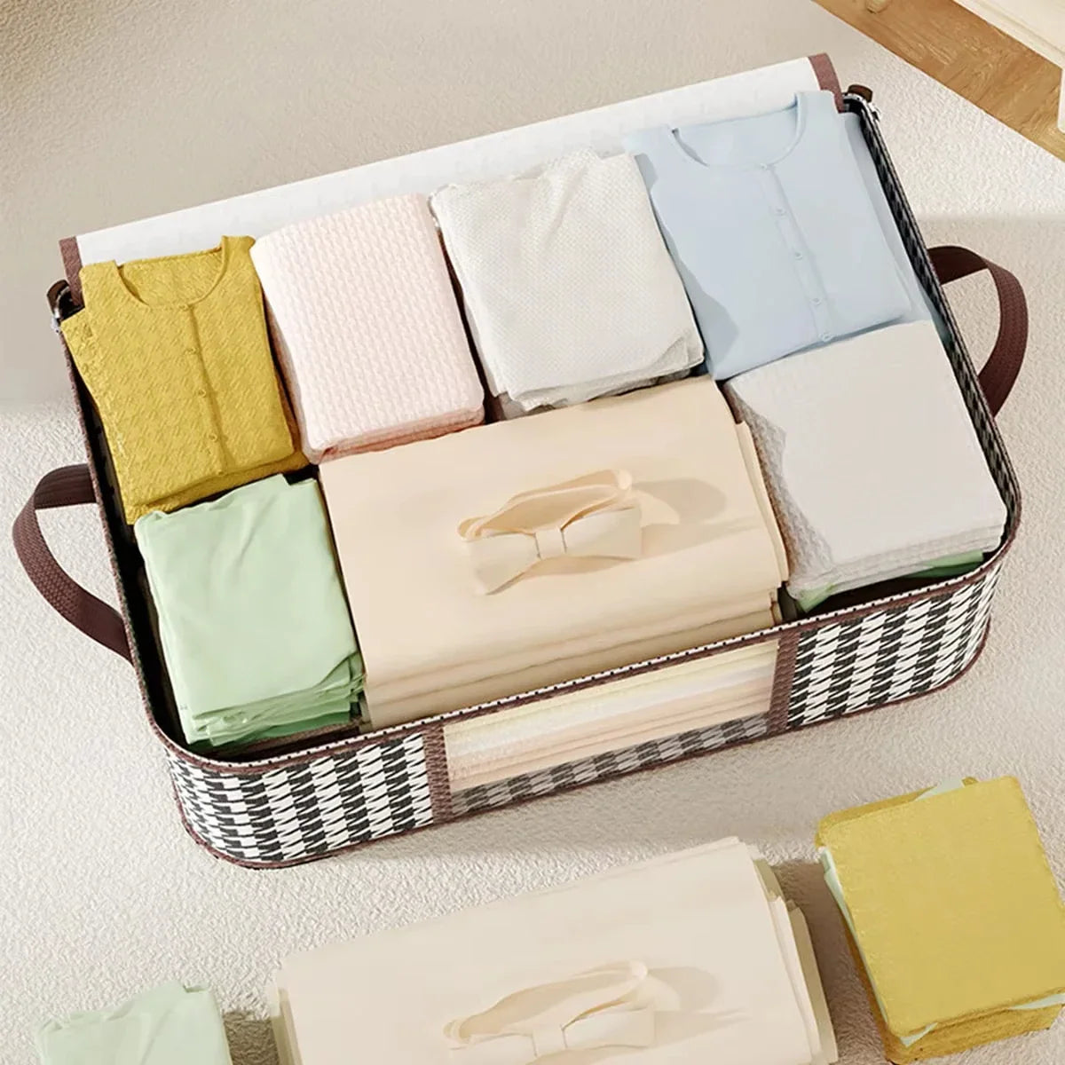 An open black and white houndstooth patterned fabric storage box filled with folded pastel-coloured clothes