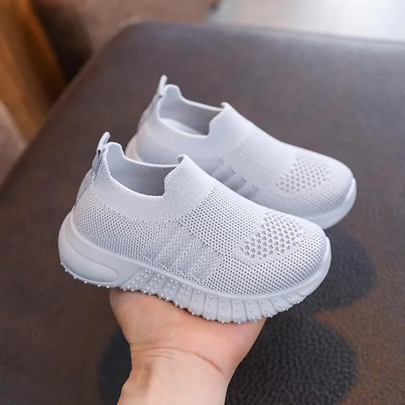 A single light grey kids knitted slip-on sneaker held in a hand