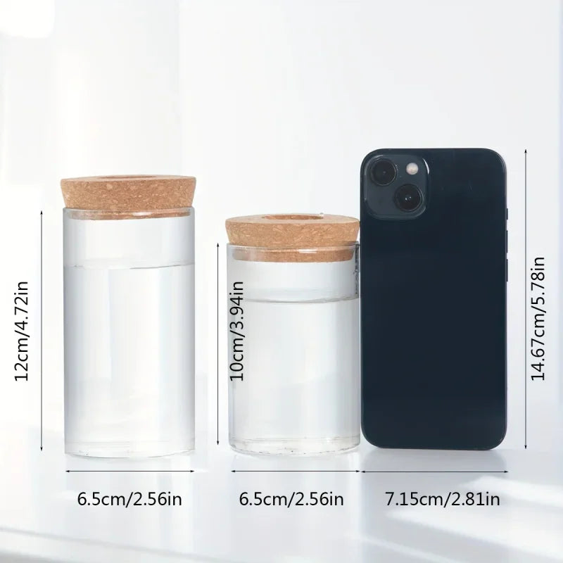 Two glass cylinders with cork lids shown with a smartphone for scale, indicating height and width dimensions