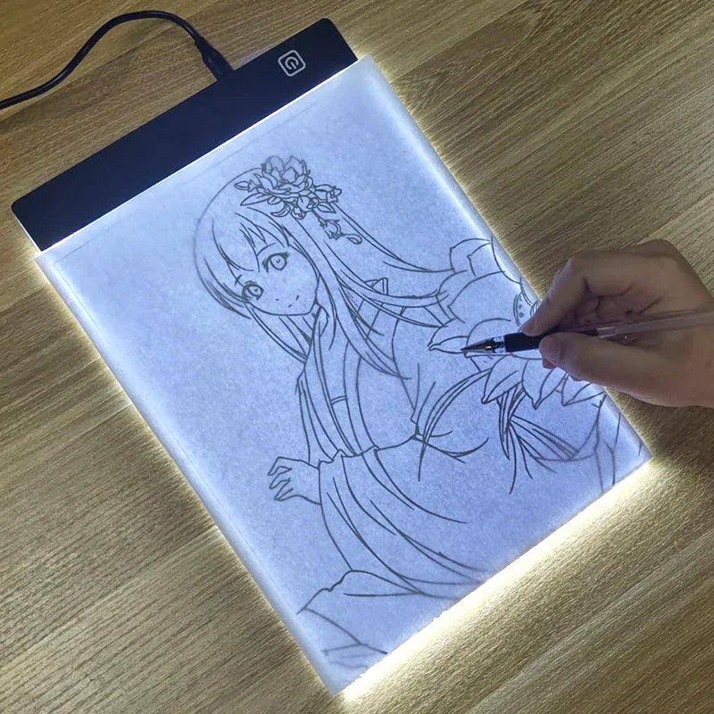 A slim, rectangular LED light tracing pad being used to sketch an anime character on a wooden desk.