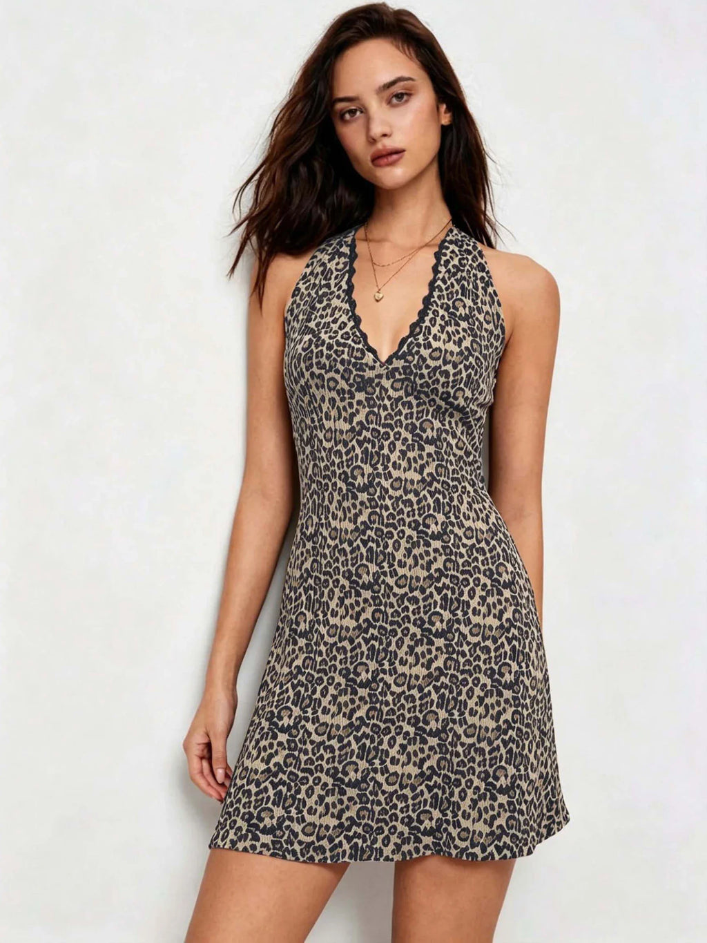 A woman posing in a leopard print V-neck halter mini dress with lace trim.