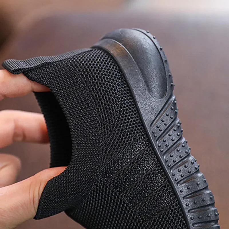 Close up of the sole and side texture of a black kids knitted slip-on sneaker held by a hand