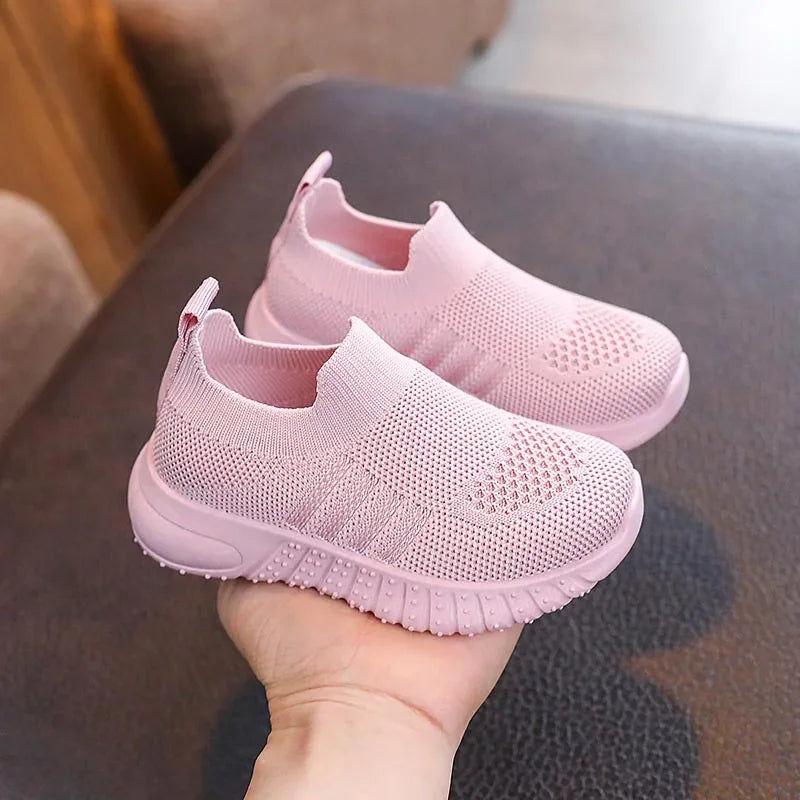 A single pink kids knitted slip-on sneaker held in a hand