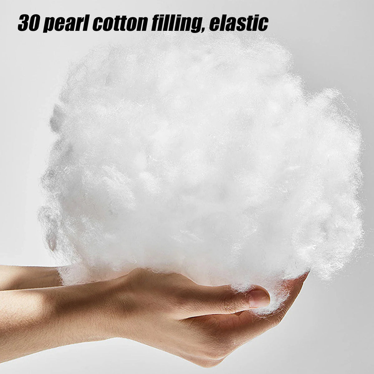 A hand holding fluffy white pearl cotton pillow stuffing material.