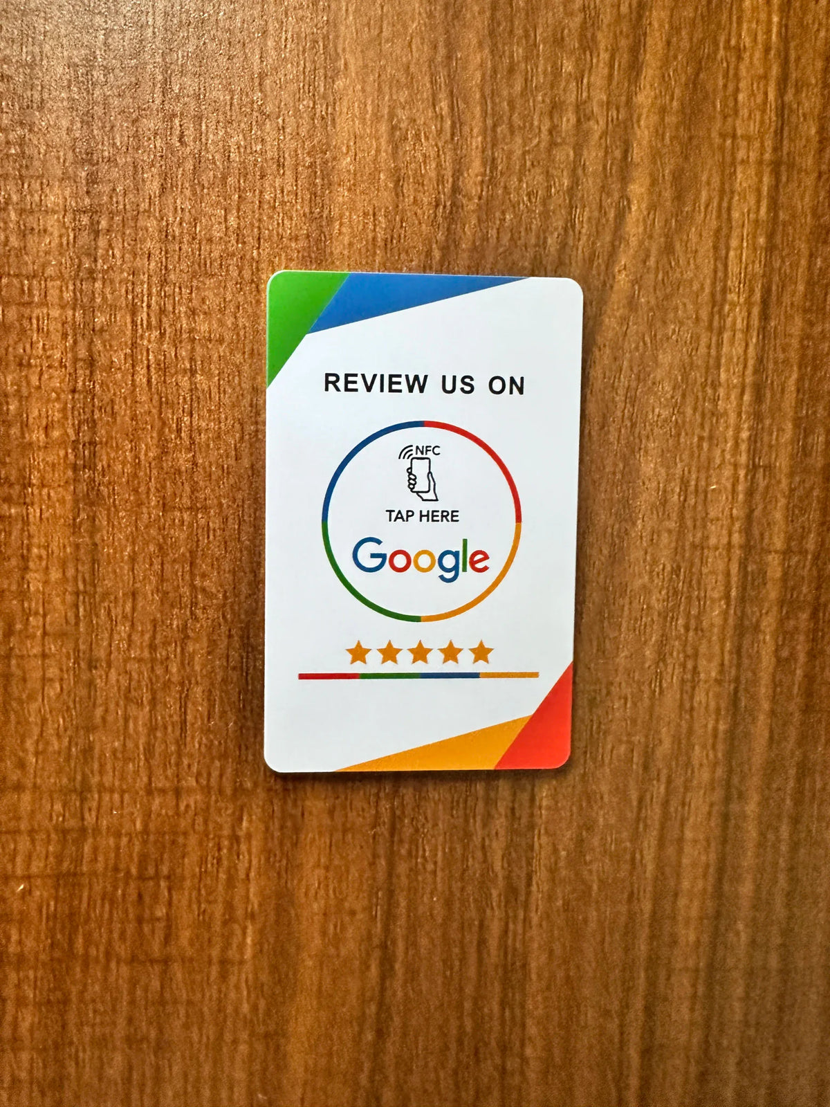 Rectangular NFC card with colorful review branding on a wooden background