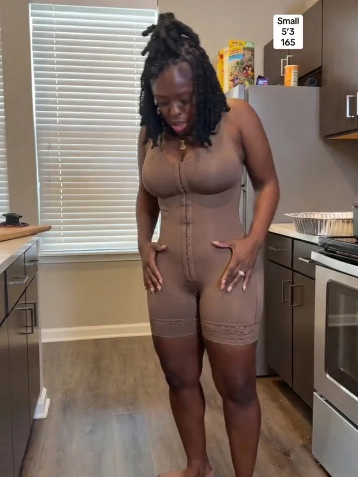 A woman wearing a brown full body shapewear bodysuit with hook-and-eye closure.