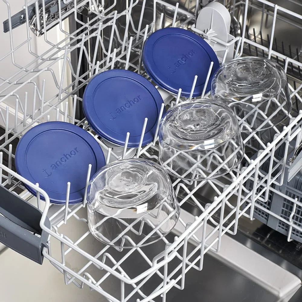 Round glass food storage containers with blue lids placed in a dishwasher rack