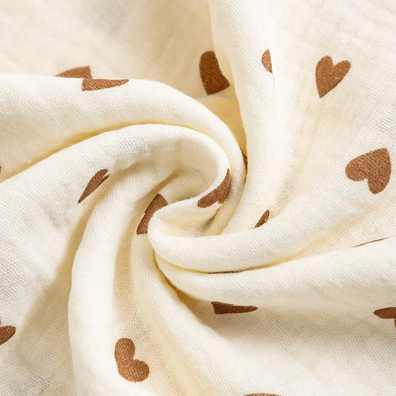 Close-up of a soft, cream-colored cotton muslin fabric with a brown heart print, showing the wrinkled texture.
