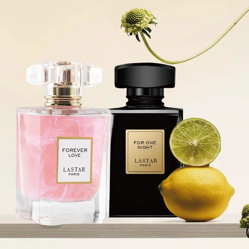 A pink perfume bottle and a black perfume bottle displayed on a shelf with fresh lemons and a flower.